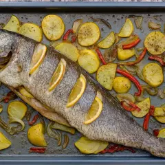Corvina al horno con patatas, pimientos y rodajas de limón en una bandeja.