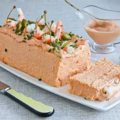 Pastel de pescado decorado con gambas, pepinillos y alcaparras. Una porción ya cortada revela su interior.