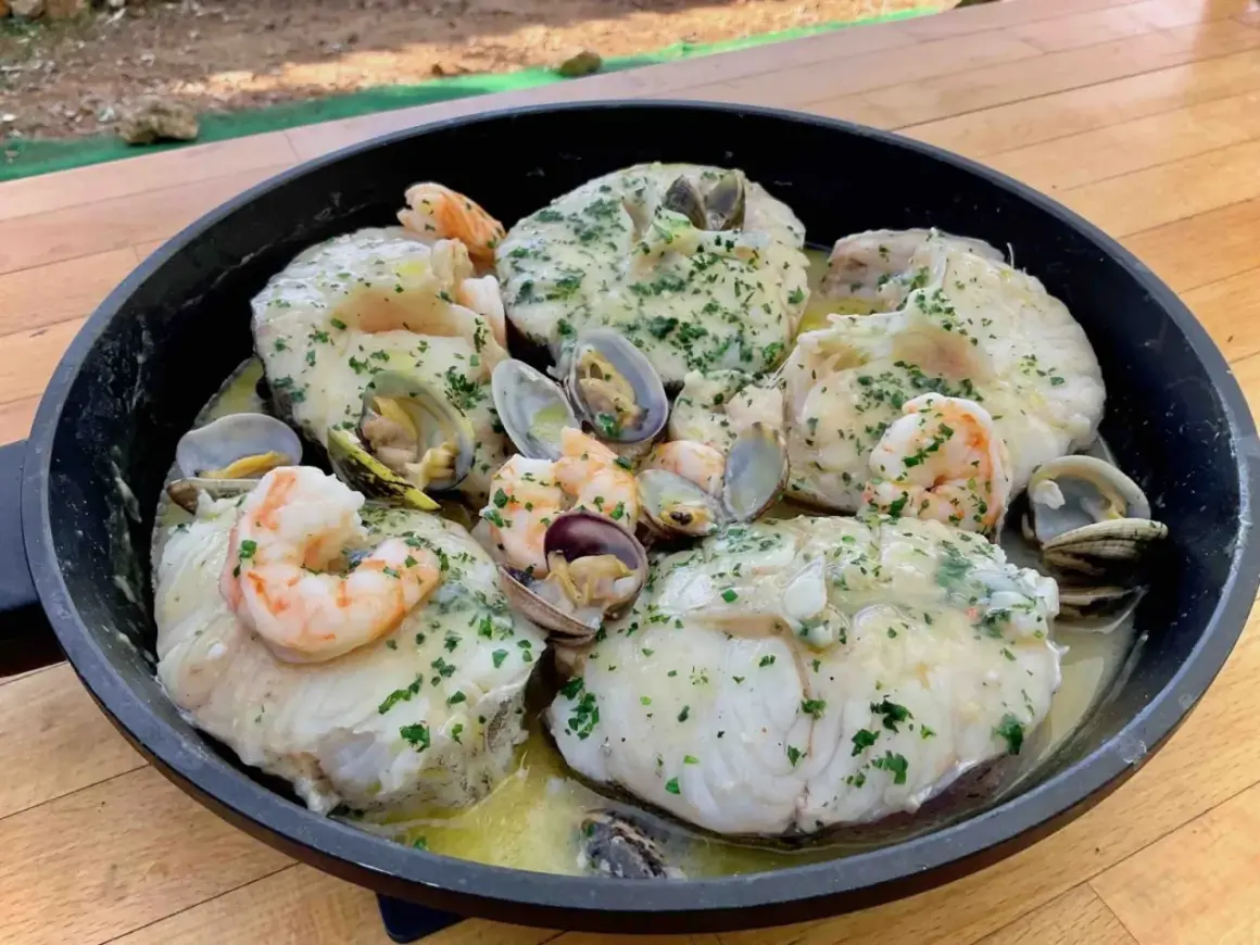 Merluza con almejas y gambas en una sartén, con perejil picado y salsa cremosa. ¡Un plato marinero delicioso!