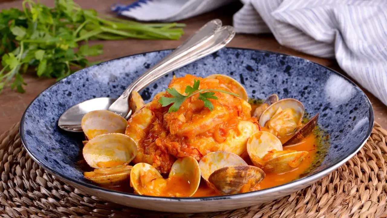 Delicioso plato de merluza con almejas y gambas en salsa, decorado con perejil fresco.